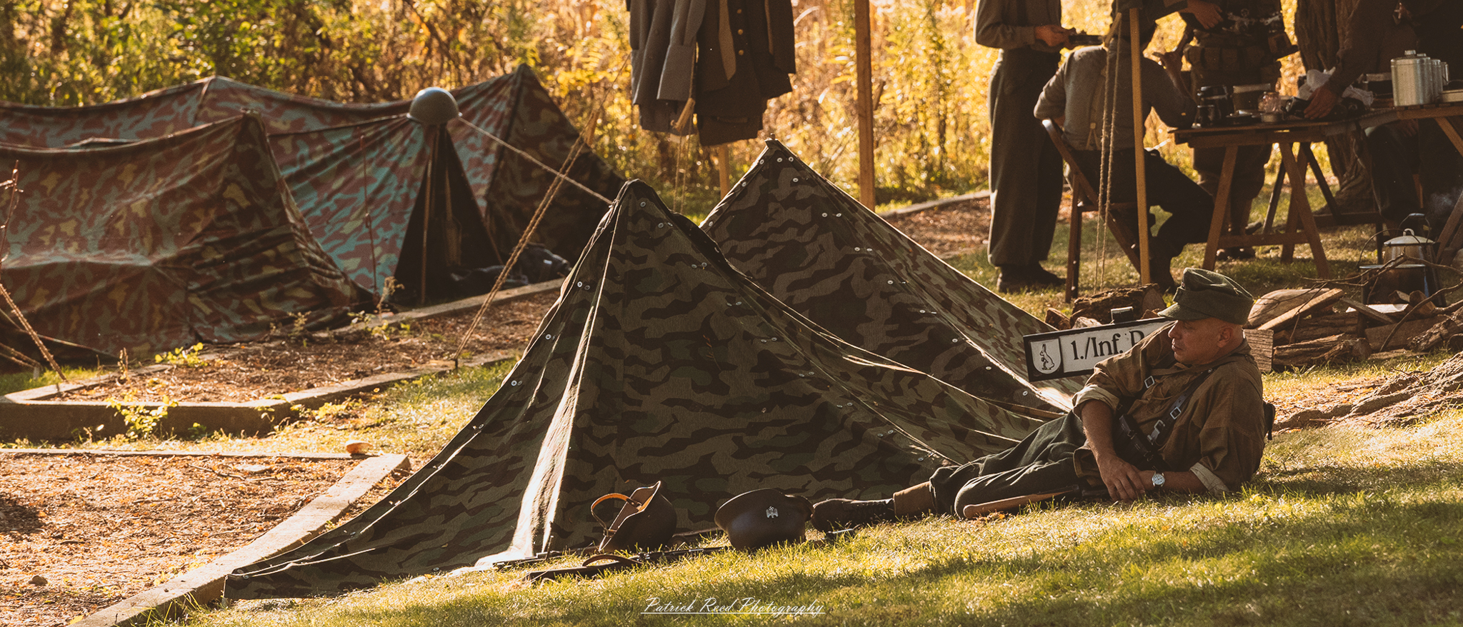 "Image of a German soldier resting in a grassy field, taking a moment to catch his breath. Dressed in a standard Wehrmacht uniform, the soldier leans against his rifle, eyes closed, with a look of exhaustion and relief on his face. The background features a serene landscape of rolling hills and soft clouds, contrasting with the tension of wartime. This moment captures the human side of soldiers amid the chaos of conflict."